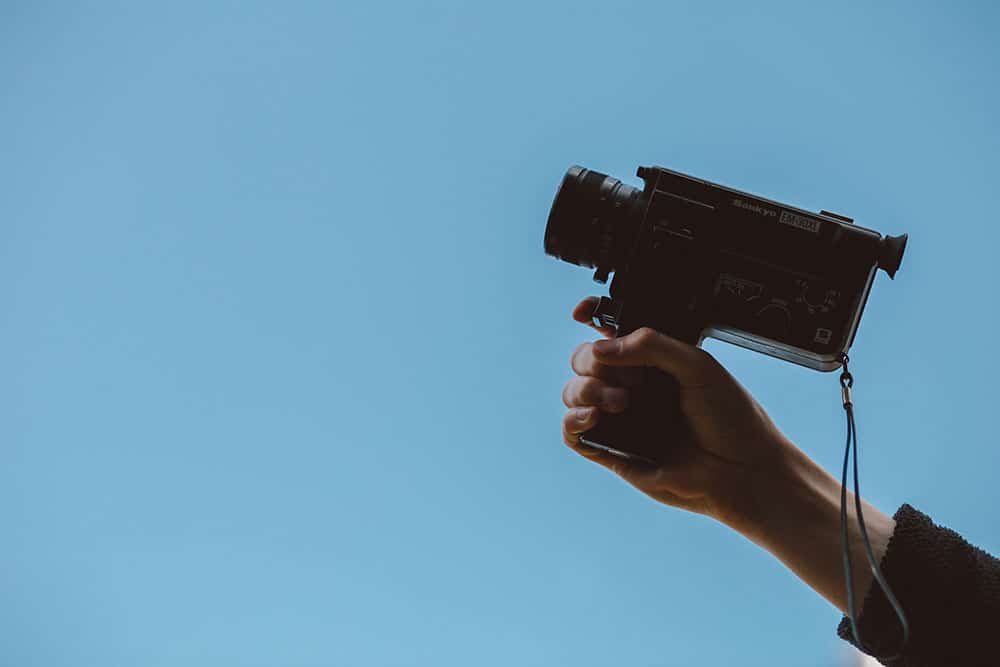 Man holding 8mm film camera against a blue background