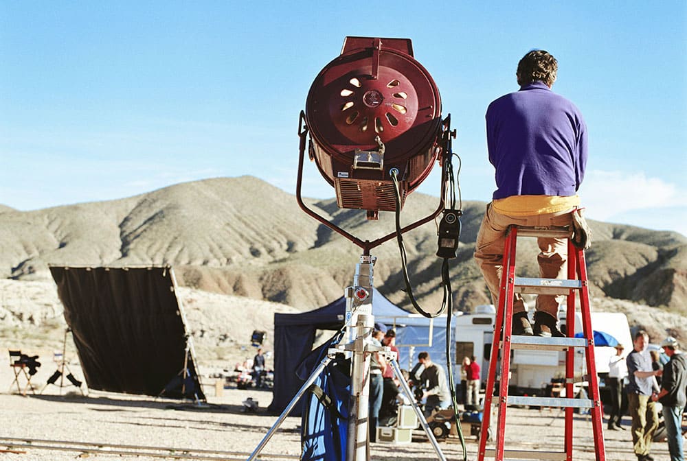 Lighting assistant on film set sitting on a ladder